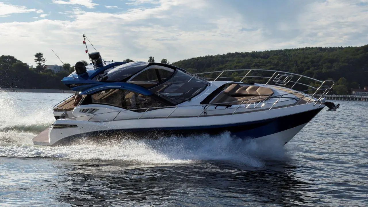 Luxury speedboat cruising on water, creating a splash, with lush green hills in the background and blue sky.