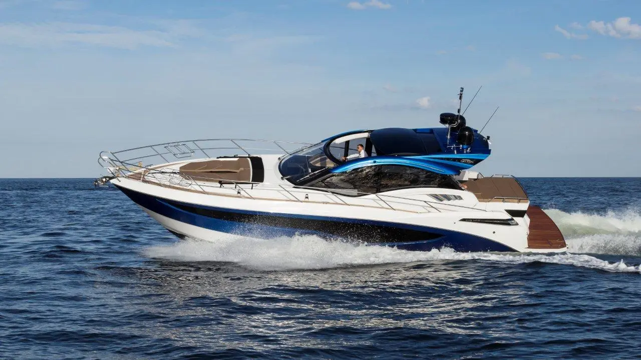 A sleek motor yacht with a blue and white design cruising on calm waters, with a captain visible at the helm.