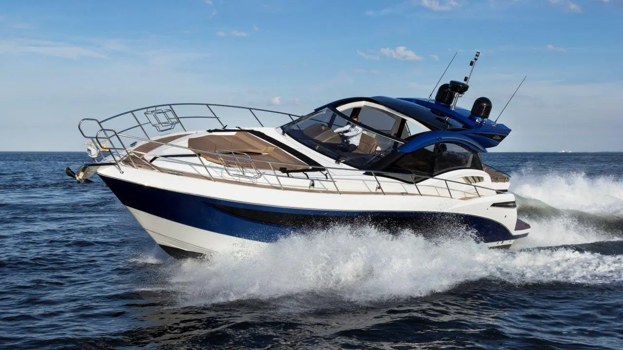 A sleek blue and white motorboat speeds through water, spray rising from the bow against a clear sky.