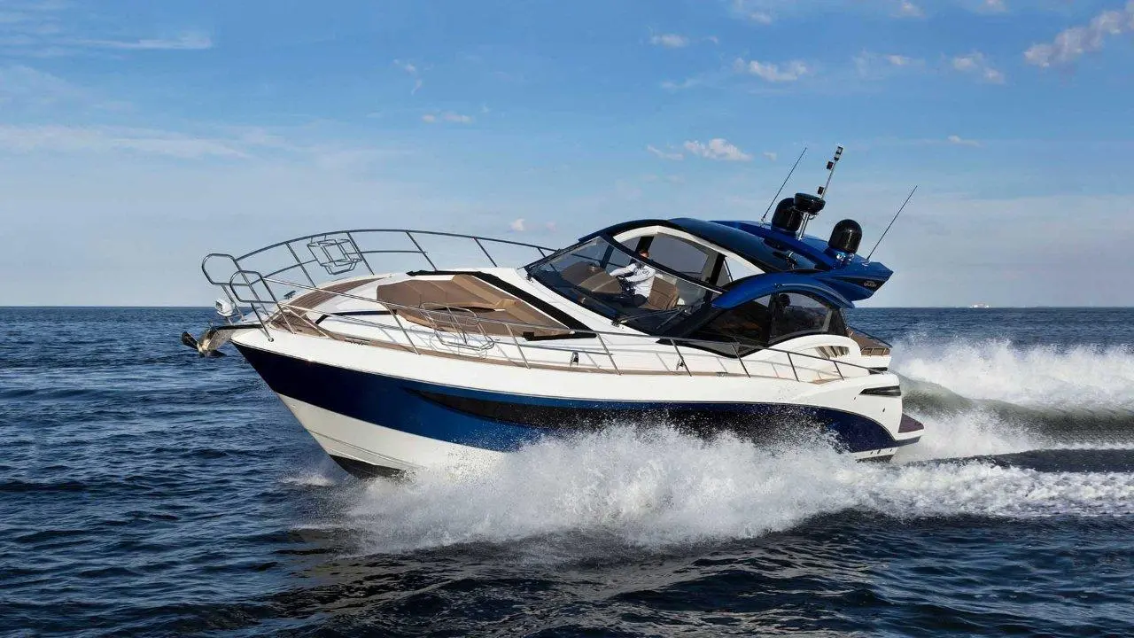 A sleek blue and white motorboat racing on the waves in clear water under a blue sky with scattered clouds.