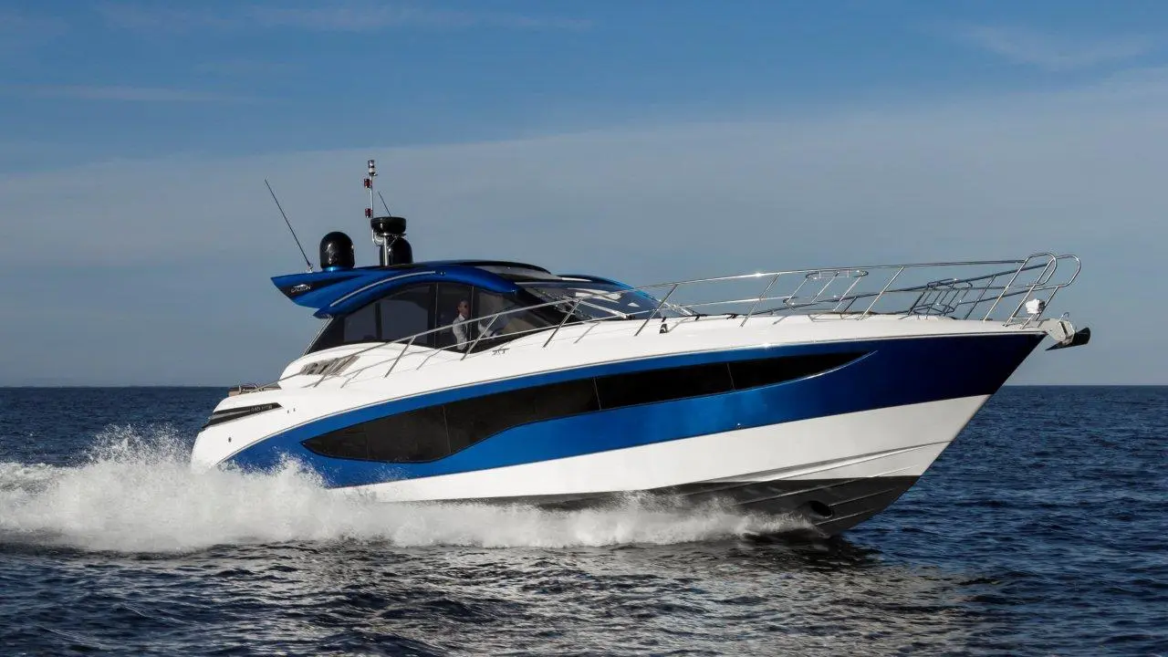 A sleek, blue and white motorboat glides through the ocean waters under a clear sky, creating a splash as it moves.