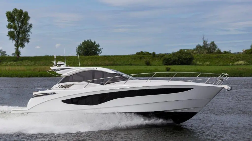 A sleek white motorboat cruises on a river, surrounded by lush green trees and a clear blue sky.