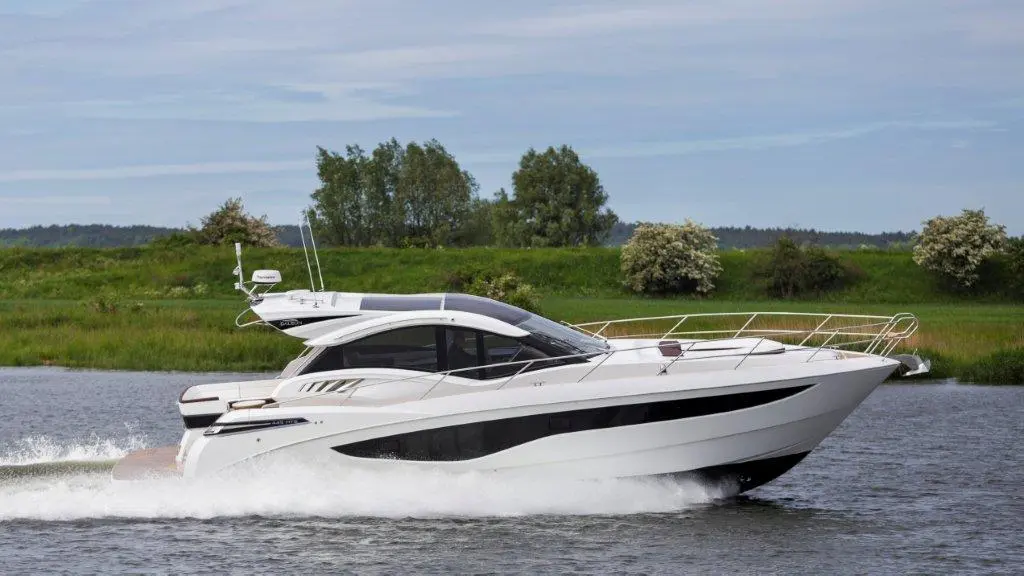 A sleek white motorboat cruises on a calm river, surrounded by green trees and blue skies, creating a serene outdoor scene.