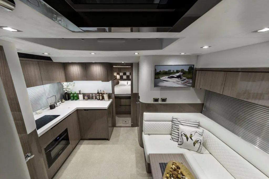 Modern yacht interior featuring a kitchen, sitting area, and a bedroom visible through an open doorway. Stylish decor includes a TV.