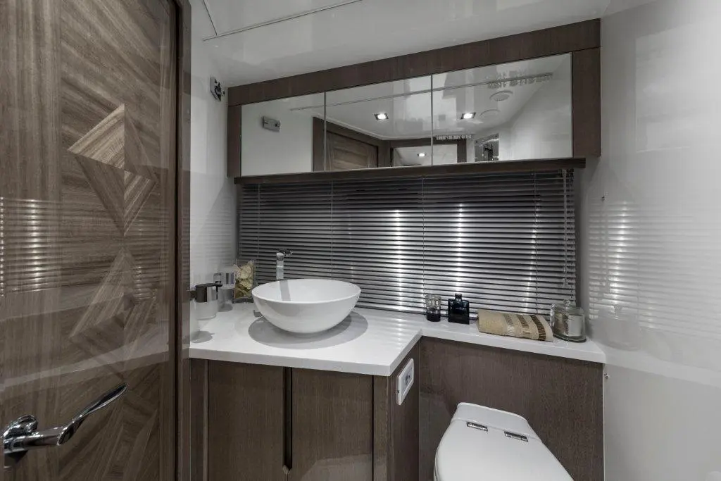 Modern bathroom with a round sink, wooden cabinetry, mirror, and striped blinds, featuring toiletries on the countertop.