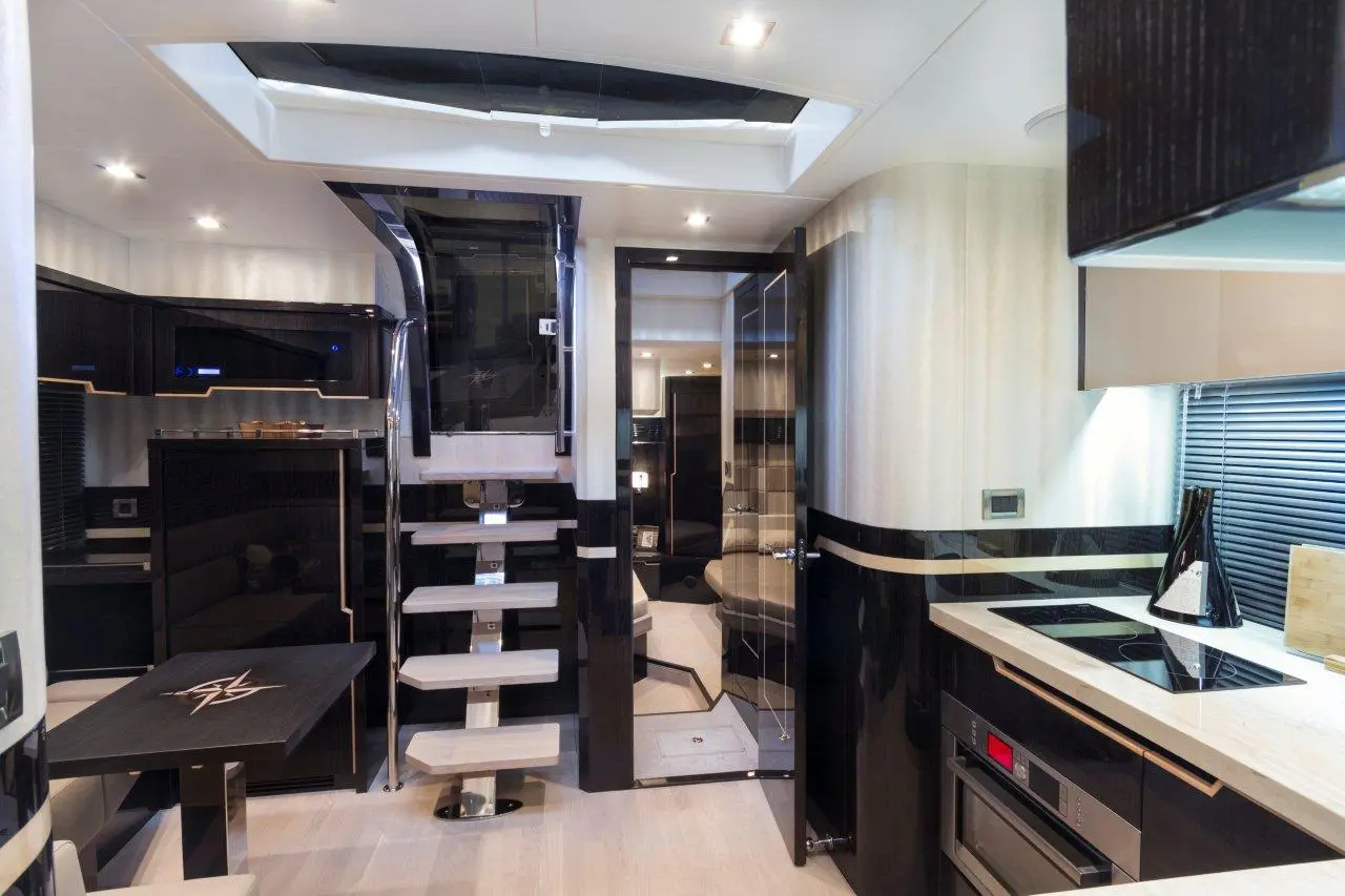 Modern yacht interior showcasing sleek kitchen, dining area, and stylish staircase. Bright lighting enhances luxurious design.