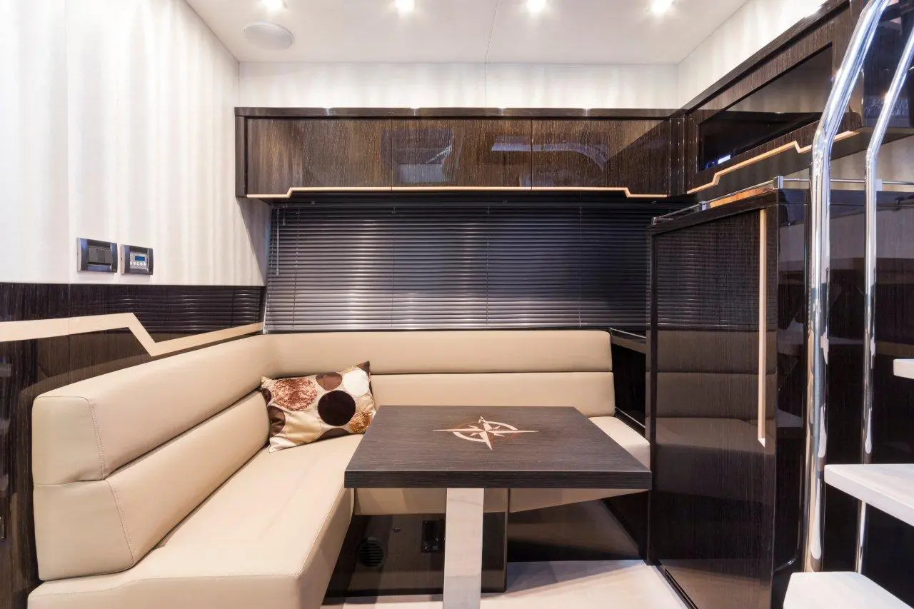 Modern yacht interior featuring a beige leather seating area, dark wood paneling, and a polished table with compass design.
