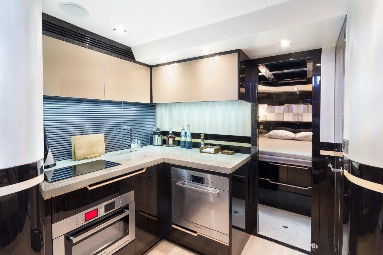 Modern yacht kitchen with black and beige cabinetry, an induction cooktop, sink, and a view into a cozy bedroom area.