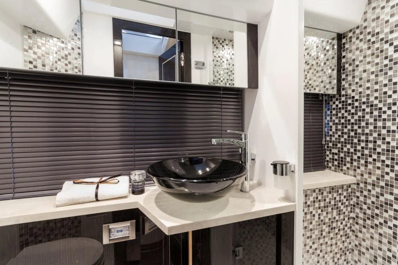 Modern bathroom with a black vessel sink, countertop, towel, and tiled wall featuring gray and beige square mosaics.
