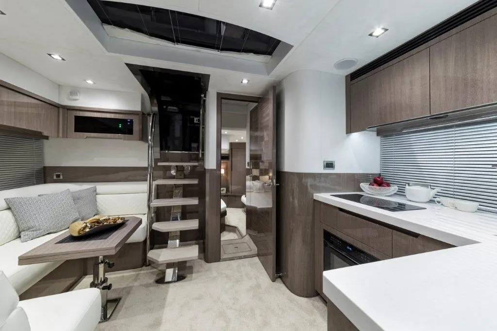Modern yacht interior featuring a staircase, kitchen area with white cabinetry, and a dining space with cushions and decor.