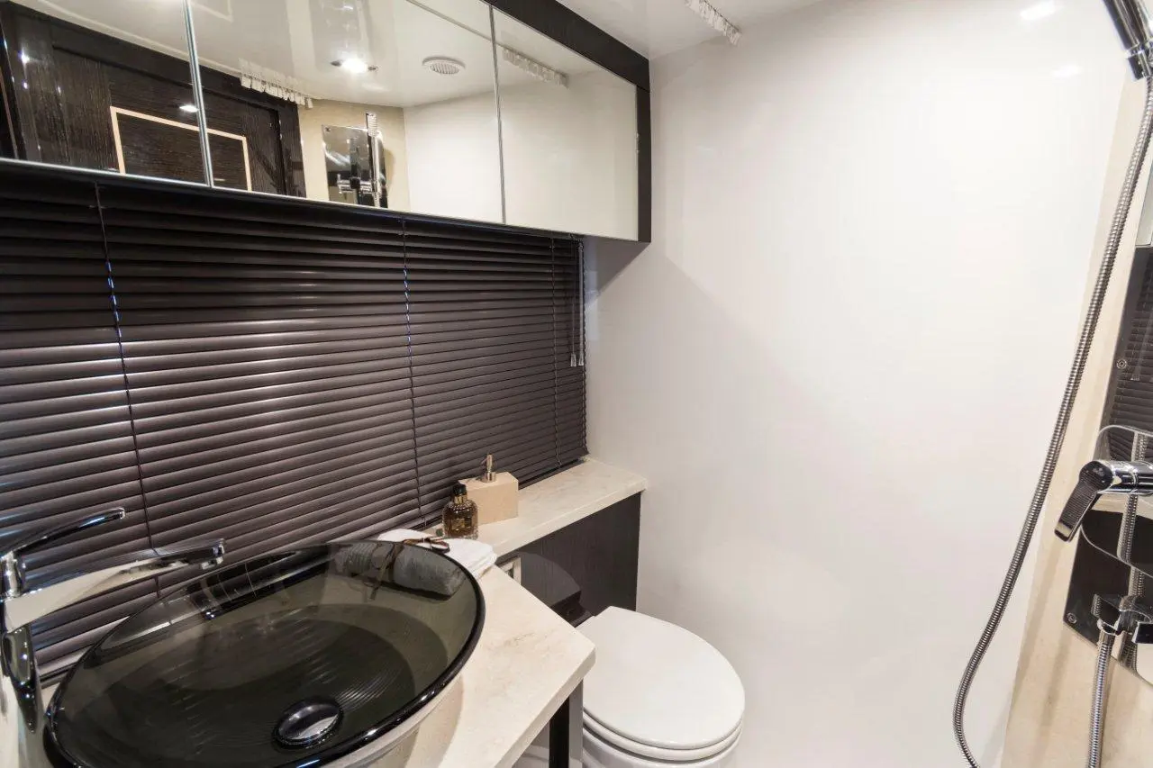 Modern bathroom featuring a black glass sink, shower, toilet, and sleek cabinetry with mirrored storage, and blinds.