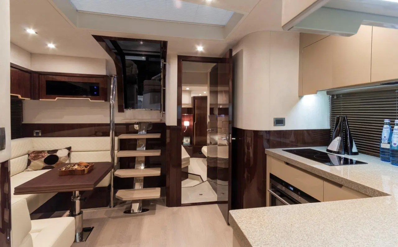 Modern yacht interior features a cozy seating area, wooden stairs, kitchenette with appliances, and stylish decor.