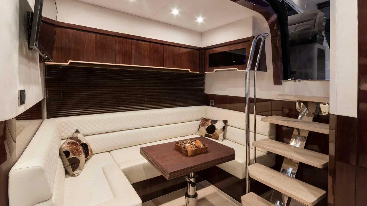 Luxury boat interior featuring a stylish lounge area with a wooden table, white seating, and a staircase leading up.