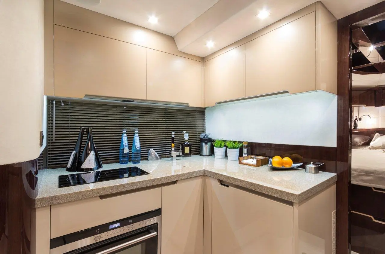 Modern kitchen with beige cabinetry, countertop, water bottles, potted plants, and a bowl of oranges, illuminated by LED lights.