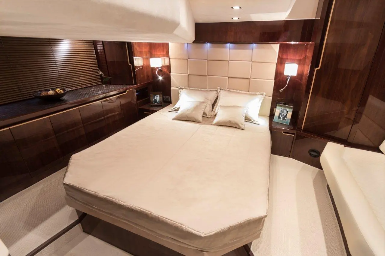 Elegant bedroom with a queen bed, beige linens, decorative pillows, wooden accents, and a bedside lamp.