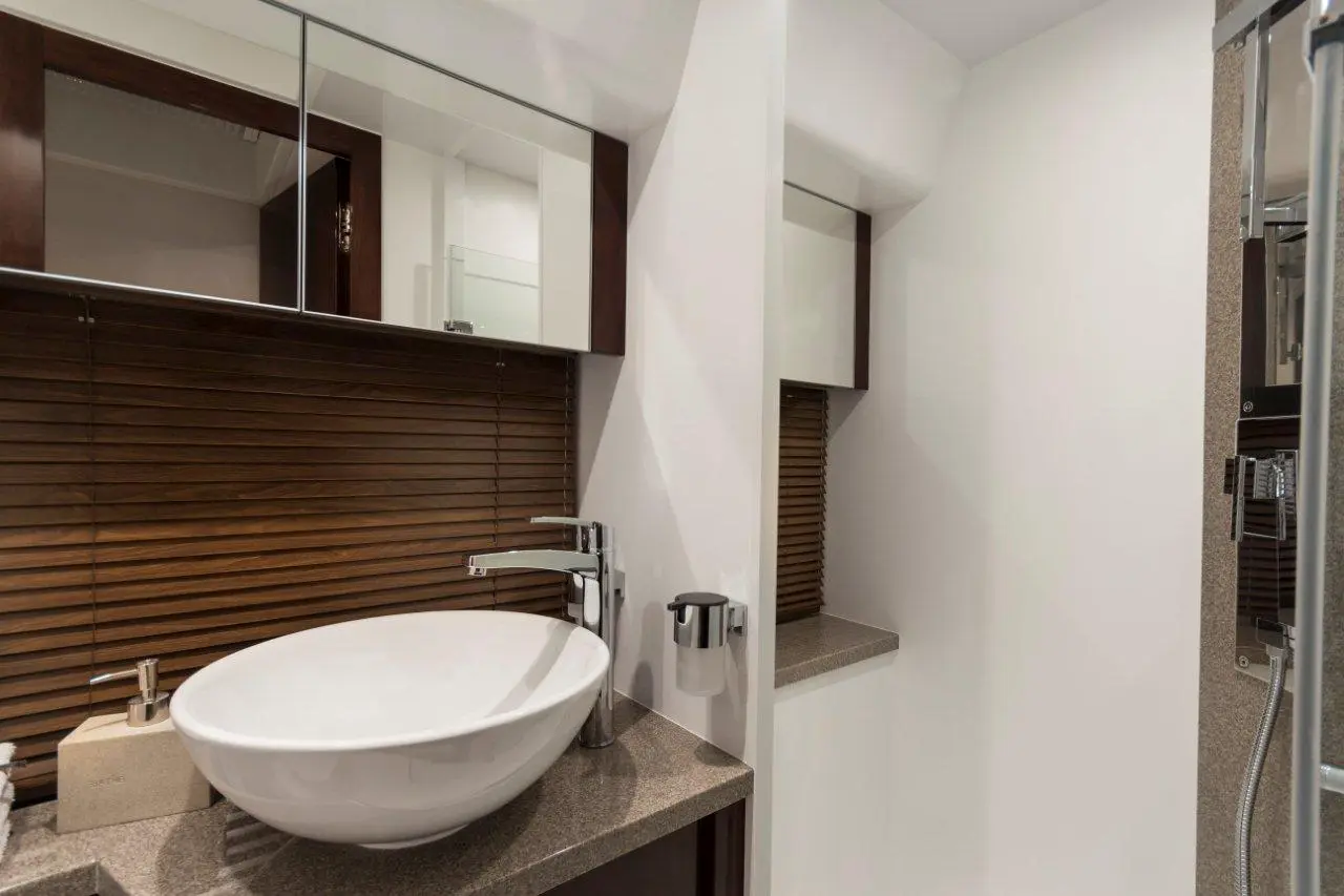 Modern bathroom with a white bowl sink, chrome faucet, wooden blinds, and mirrors above dark wood cabinetry.