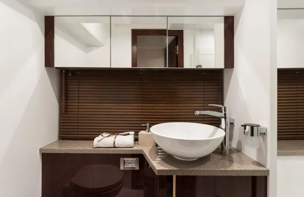 Modern bathroom featuring a round sink, countertop with a towel, and wooden blinds. Mirrors above enhance the spacious look.