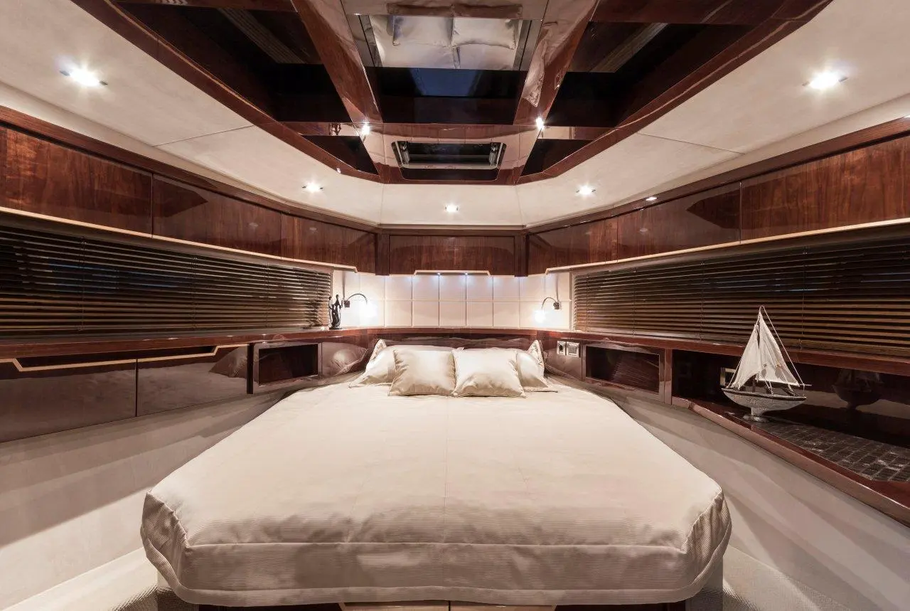 Luxury boat cabin featuring a double bed, wooden furnishings, and ambient lighting, with a model sailboat on the shelf.