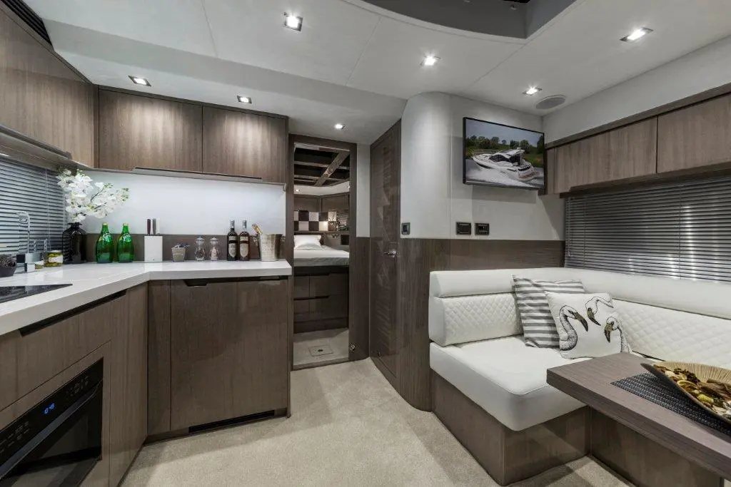 Modern boat interior featuring a kitchen area, seating with decorative pillows, and a small TV displaying a boat image.