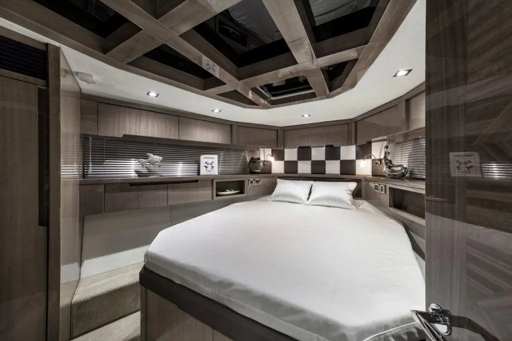 Cozy yacht cabin with a queen-size bed, wooden accents, modern lighting, and decorative elements on the shelves.