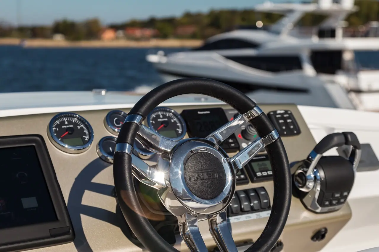 Boat dashboard featuring a steering wheel, gauges, a touchscreen display, and audio controls, with a background of water and yachts.