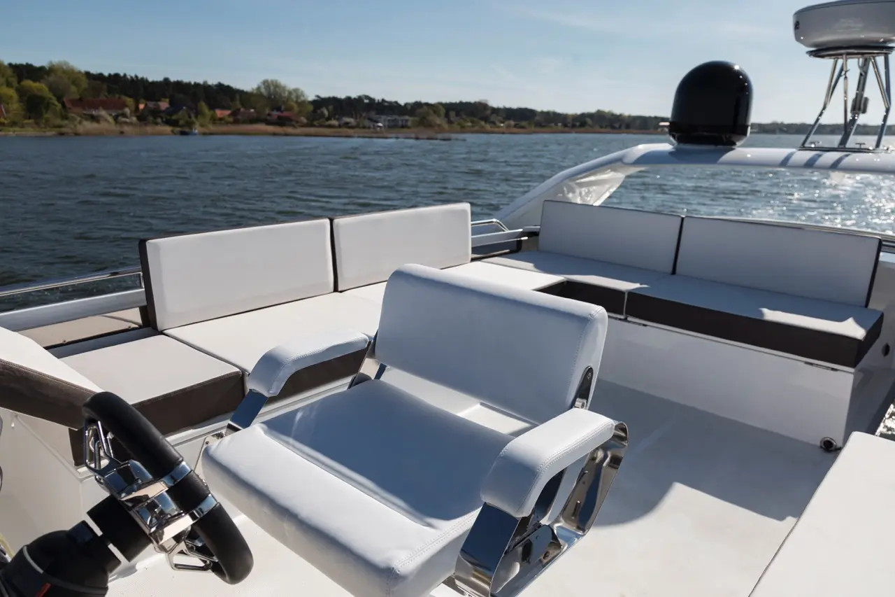 Luxury boat seating area with a white captain's chair, surrounding plush gray and white cushions and a scenic water view.