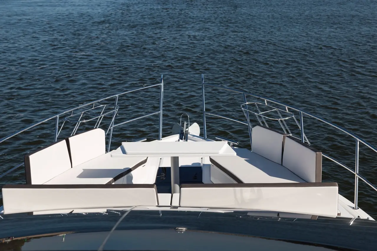 View from the bow of a yacht, featuring white seating and a table, overlooking calm water under clear skies.