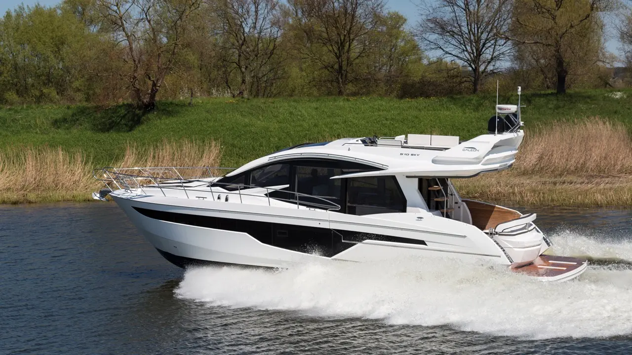 A sleek white motorboat speeds across a calm waterway, with lush greenery along the shore and a clear blue sky above.