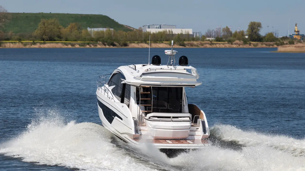 A luxury motor yacht speeds through calm waters, creating a spray; modern design with a spacious deck is visible.
