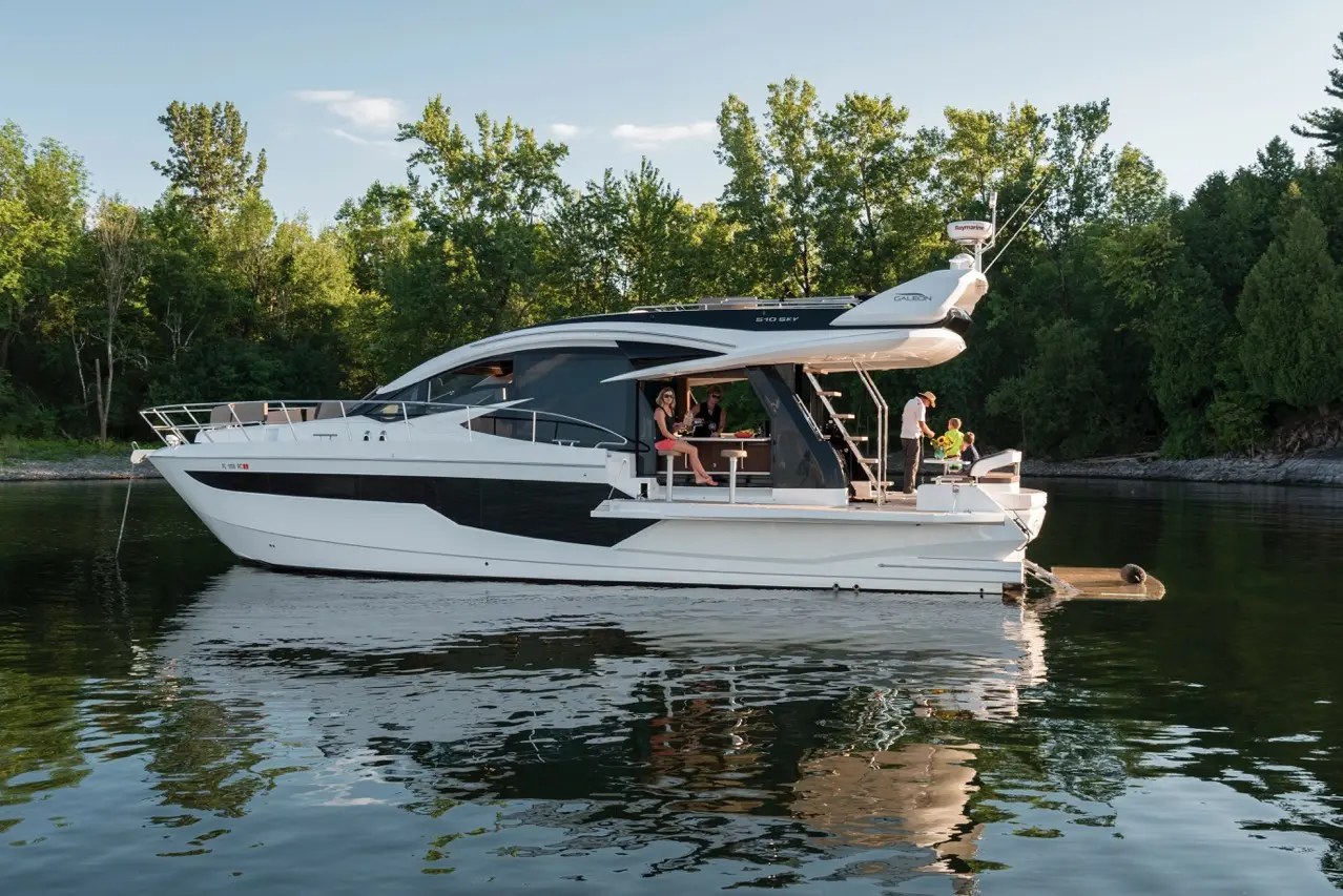 A luxury motor yacht with people aboard, enjoying the water, surrounded by trees and a calm lake.