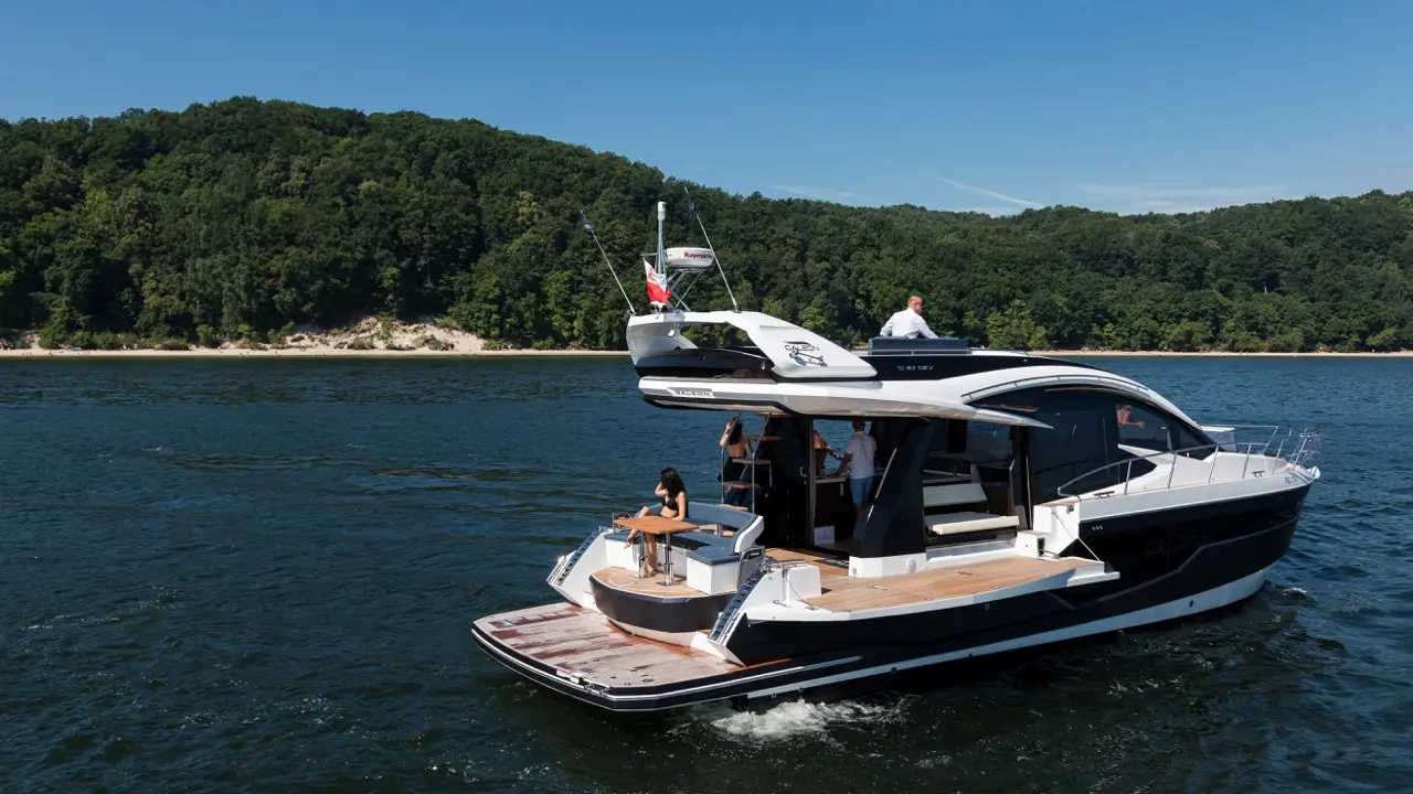 A modern motorboat with a sun deck on a lake, featuring people socialising and enjoying the sunny day.