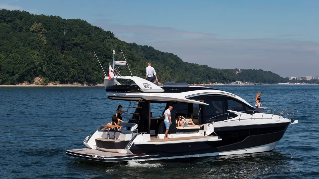 A luxury boat cruising on a serene lake with passengers lounging and enjoying the sun, surrounded by green hills.