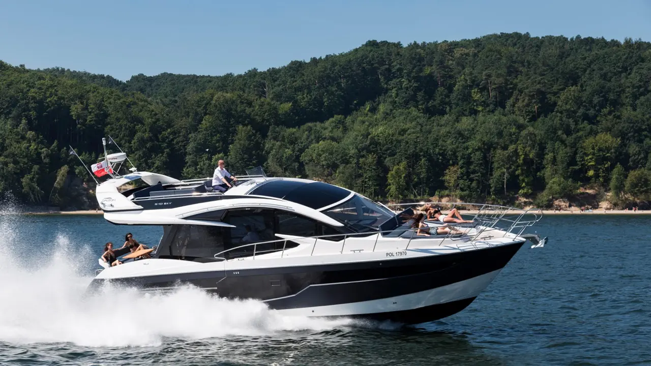 A luxury motor yacht speeds across a lake, with passengers relaxing on deck and green hills in the background.