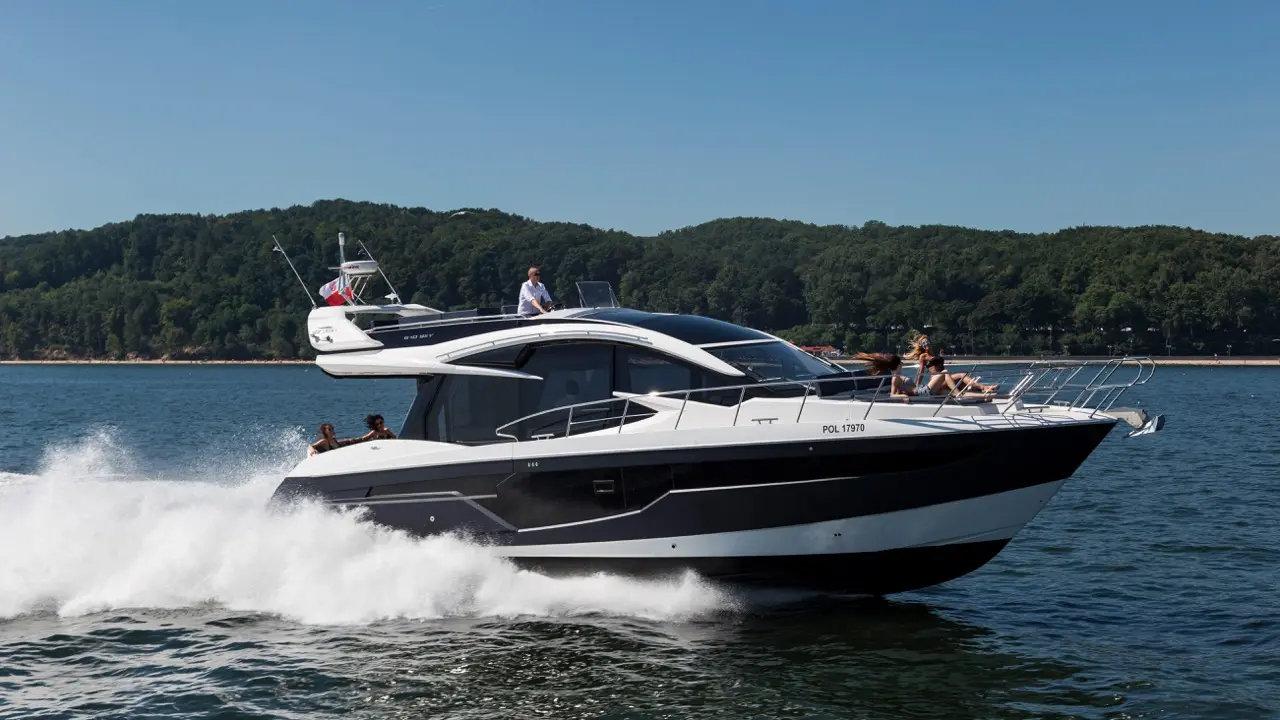 A sleek motorboat speeds across water, with people enjoying the sun on deck, surrounded by green hills and clear skies.