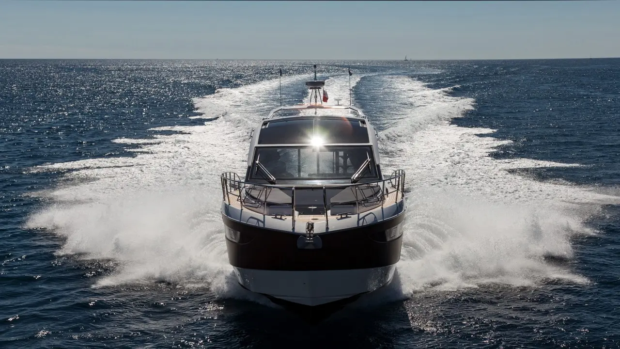 A sleek motor yacht navigates a sparkling ocean, creating white wake trails under a clear blue sky.