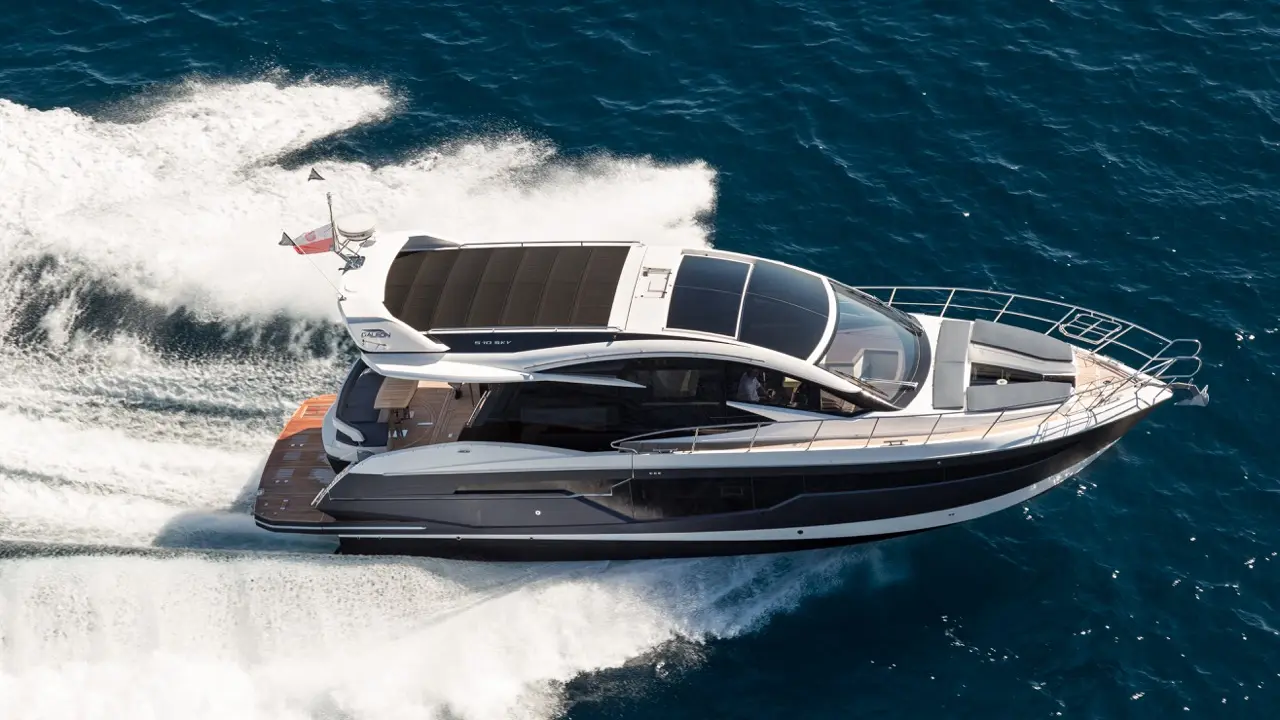 A sleek motor yacht with solar panels glides over deep blue waters, leaving frothy waves in its wake.