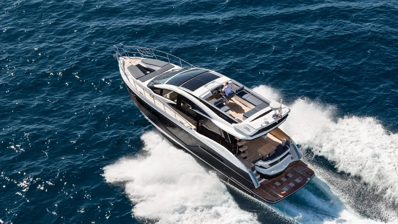 A luxury motor yacht navigates through blue waters, showcasing a sleek design and spacious deck areas.