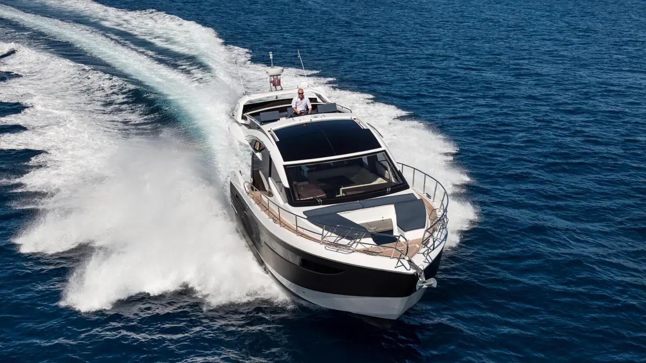 A sleek motor yacht speeds through deep blue waters, leaving a white foam trail behind, with a captain at the helm.