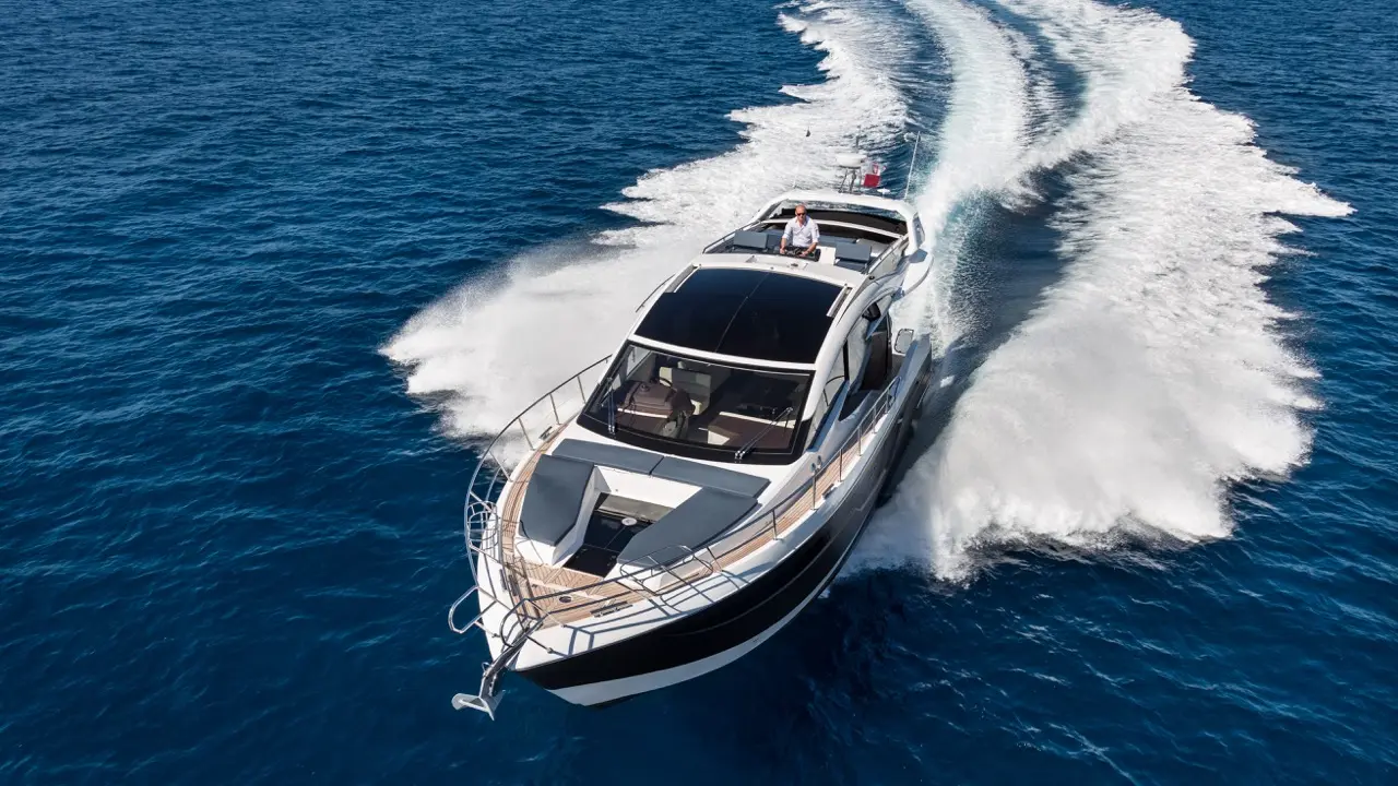 A luxury motor yacht speeds across azure waters, leaving white wake trails, with a captain at the helm.