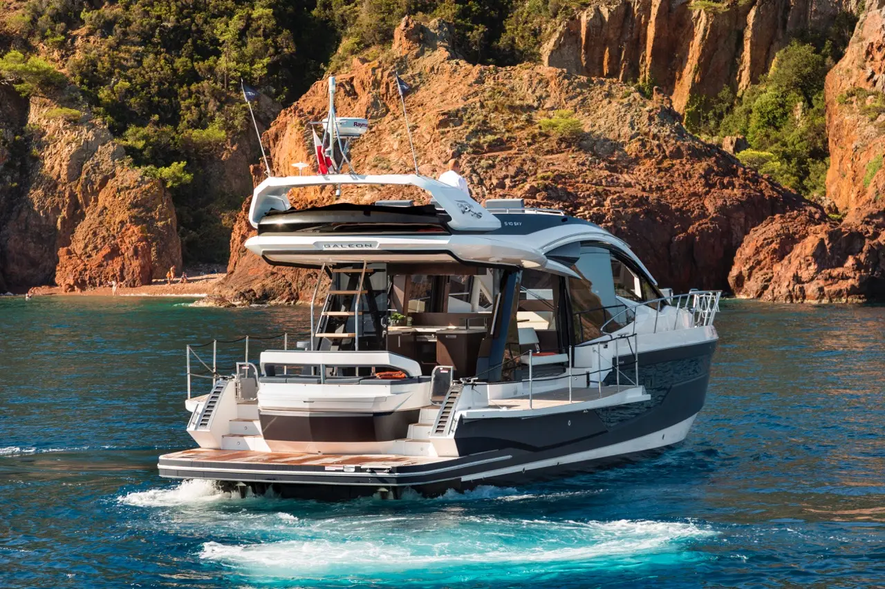 Luxury motor yacht cruising on clear blue water near rugged cliffs, showcasing modern design and spacious deck areas.
