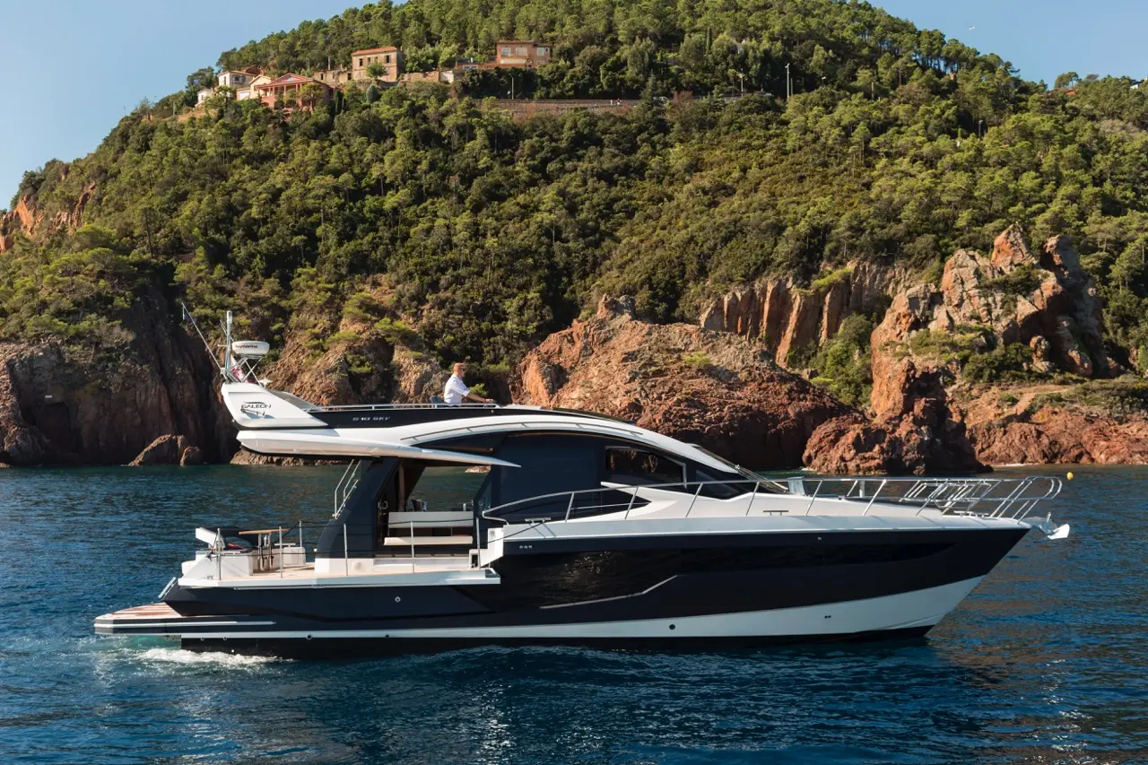 Luxury motor yacht cruising in calm waters with a scenic rocky coastline and lush greenery in the background.