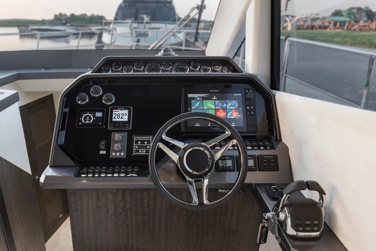 Boat cockpit displaying a modern steering wheel, dashboard gauges, touchscreen, and communication equipment.