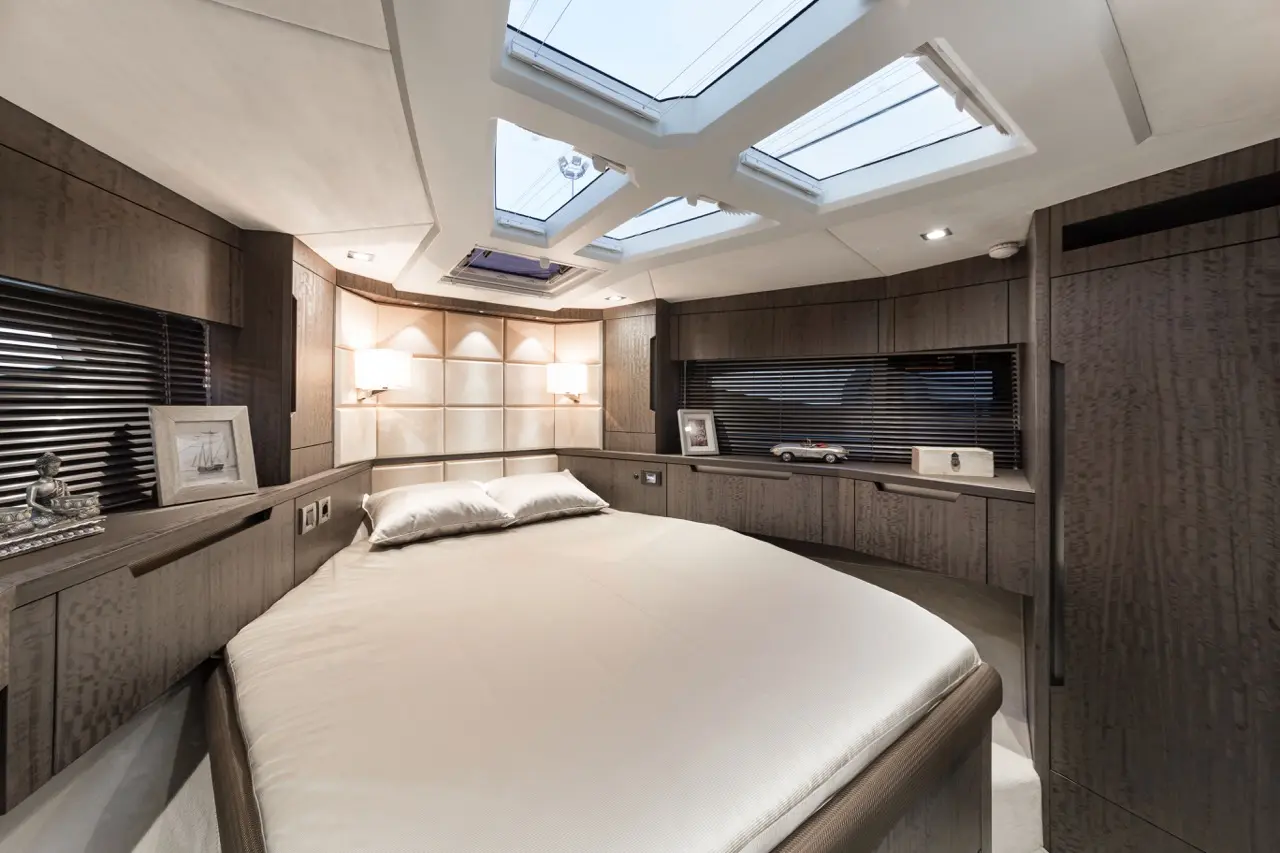 Modern yacht interior featuring a queen-sized bed, skylights, wooden cabinetry, and decorative accents, creating a serene atmosphere.