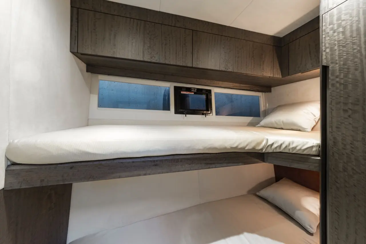 Interior view of a compact cabin with two beds, storage cabinets, and a window showing rain-streaked glass.