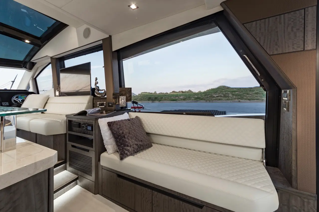 Interior of a luxury yacht featuring a plush white bench seat, modern decor, and large windows overlooking a scenic view.