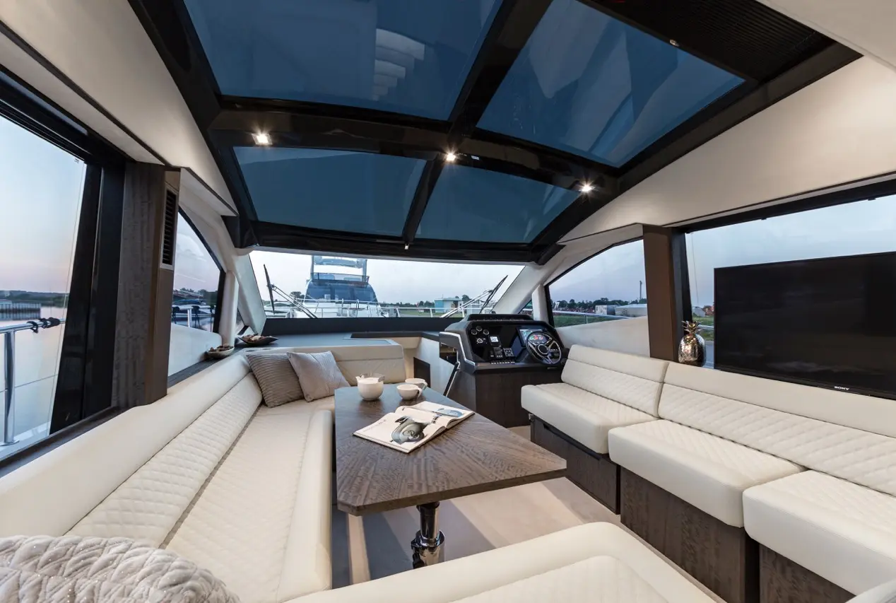 Luxurious yacht interior featuring modern seating, a wood table, and a view of the water from large windows at sunset.