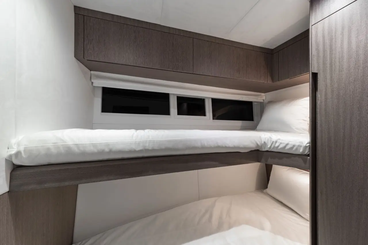 Modern bunk bed design in a compact space, featuring two white mattresses, wood paneling, and a small window.