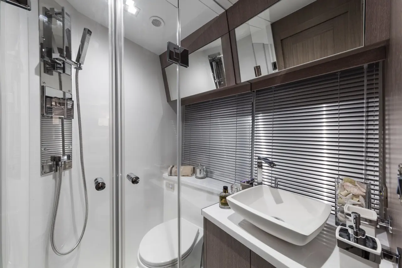 Modern bathroom featuring a glass shower, sleek toilet, white basin, and mirrored cabinets with horizontal blinds.