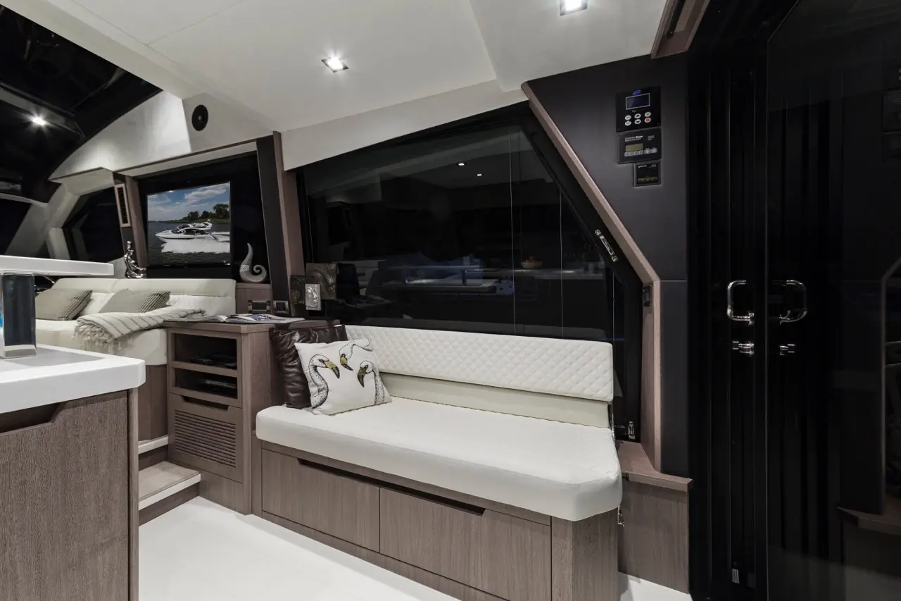 Modern boat interior with a white seating area, decorative pillow, visible TV, and stylish cabinetry. Bright, elegant design.
