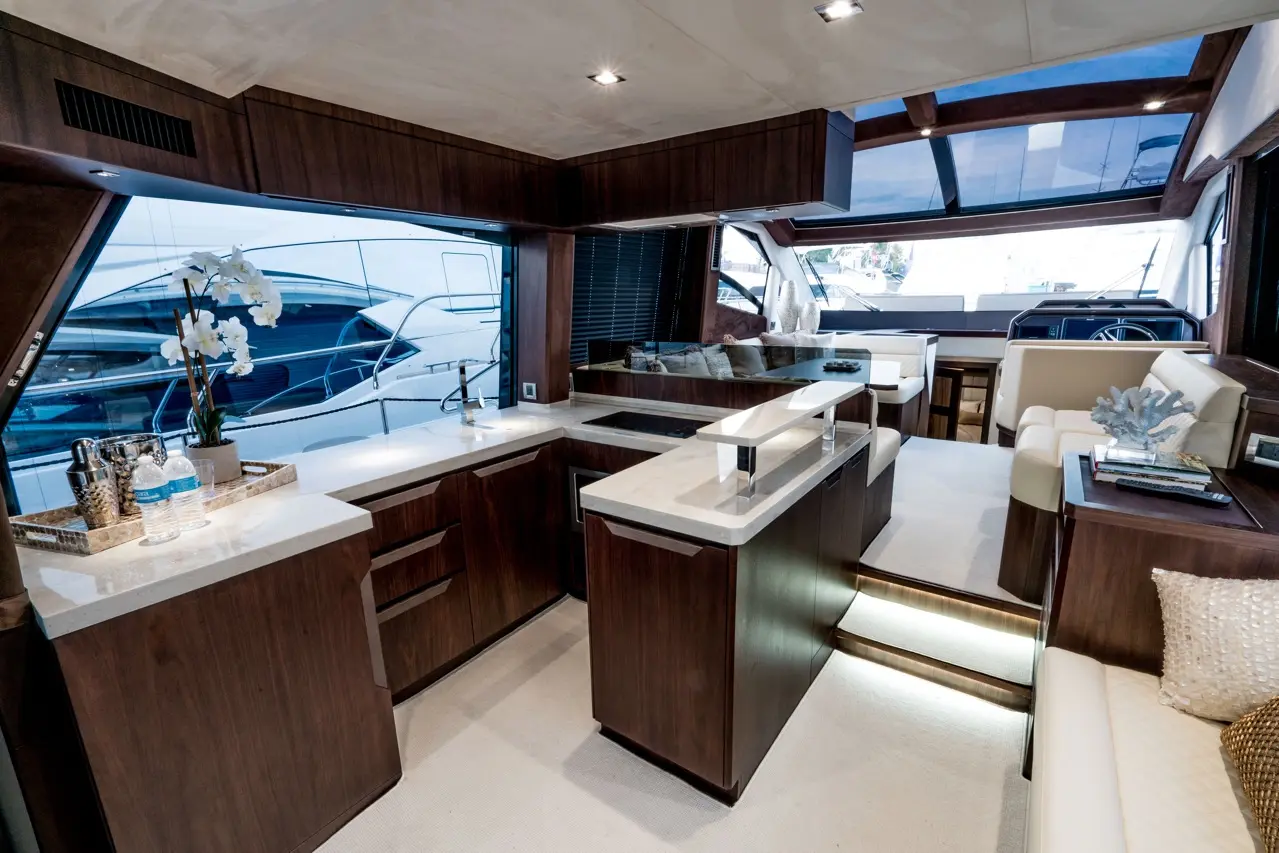Luxurious yacht interior featuring a modern kitchen, lounge area, potted orchids, and large windows with views of other boats.